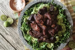 Stone bowl of spiced grilled meat chunks over fresh greens